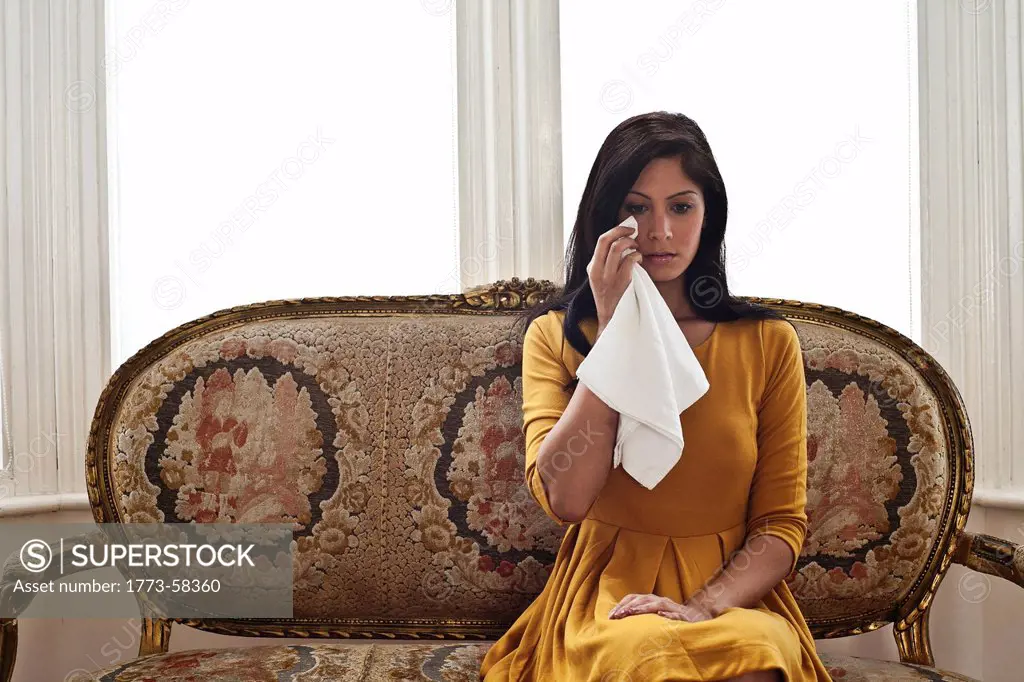 Woman wiping her eyes on sofa