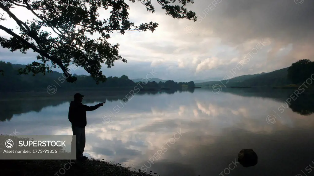 Silhouette of a man enjoying view over a still lake with cloud reflections during twilight hours