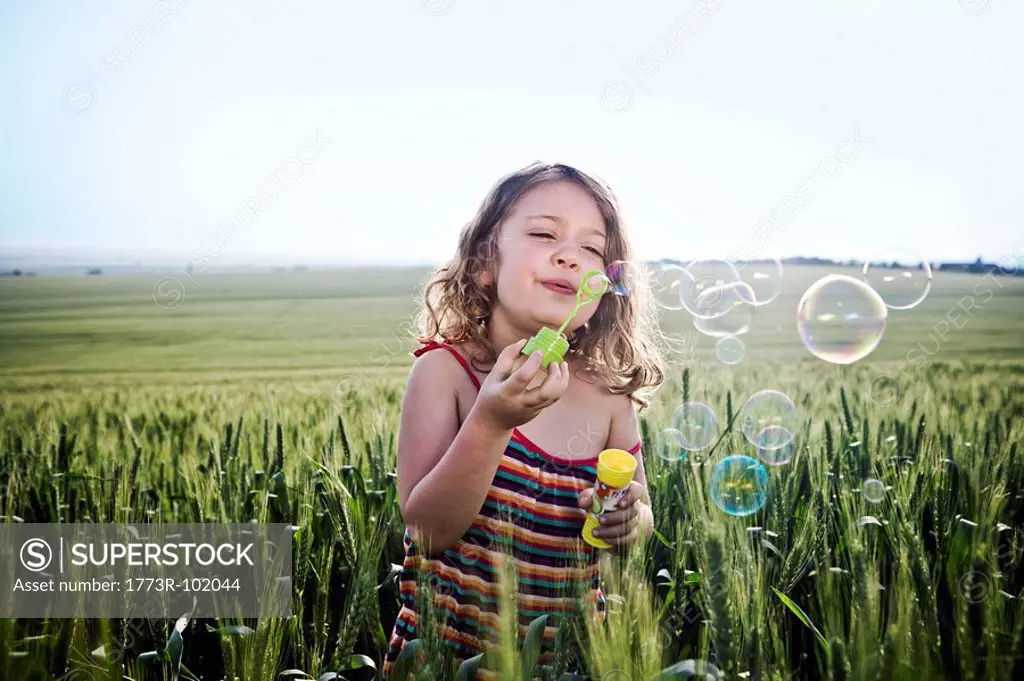 Girl blowing bubbles in wheat field