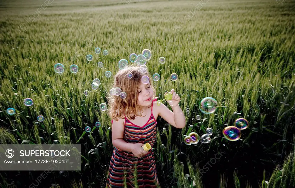 Girl blowing bubbles in wheat field