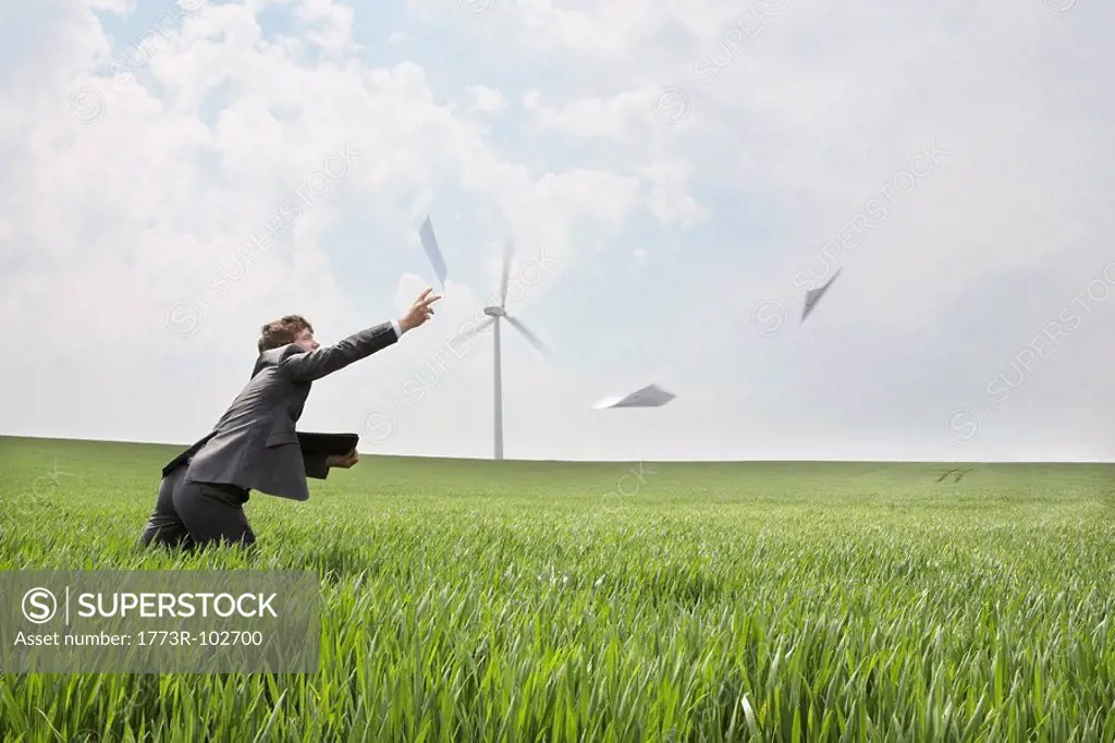 Businessman chasing papers on wind farm