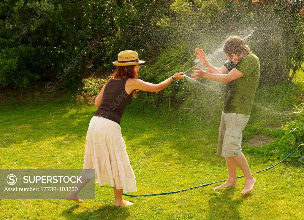 Woman spraying man with garden hose
