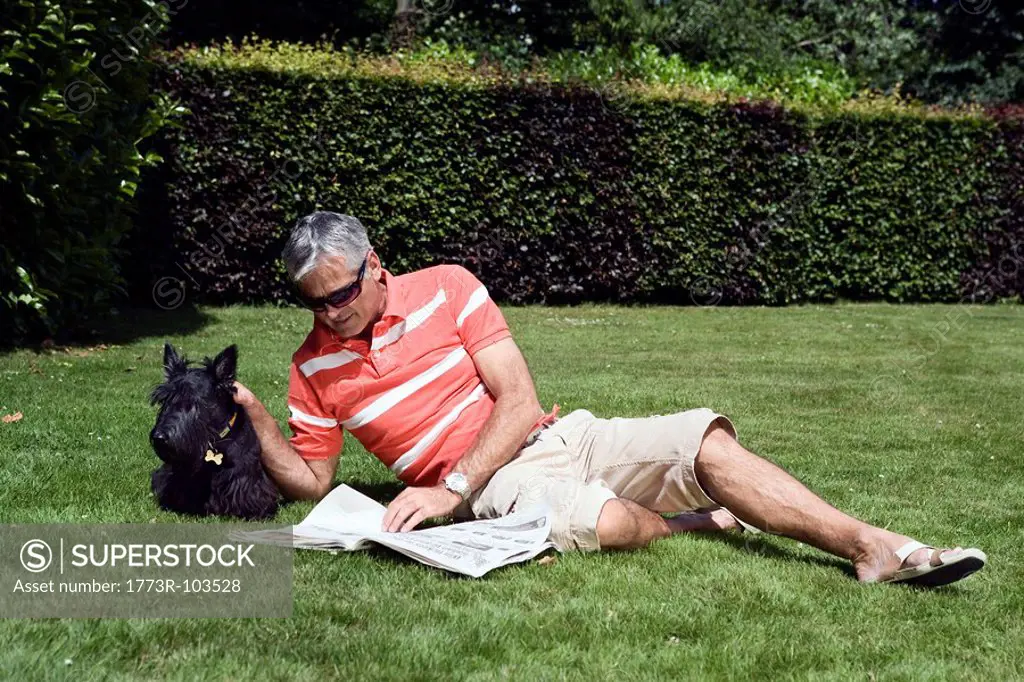 Mature man laying on grass reading paper