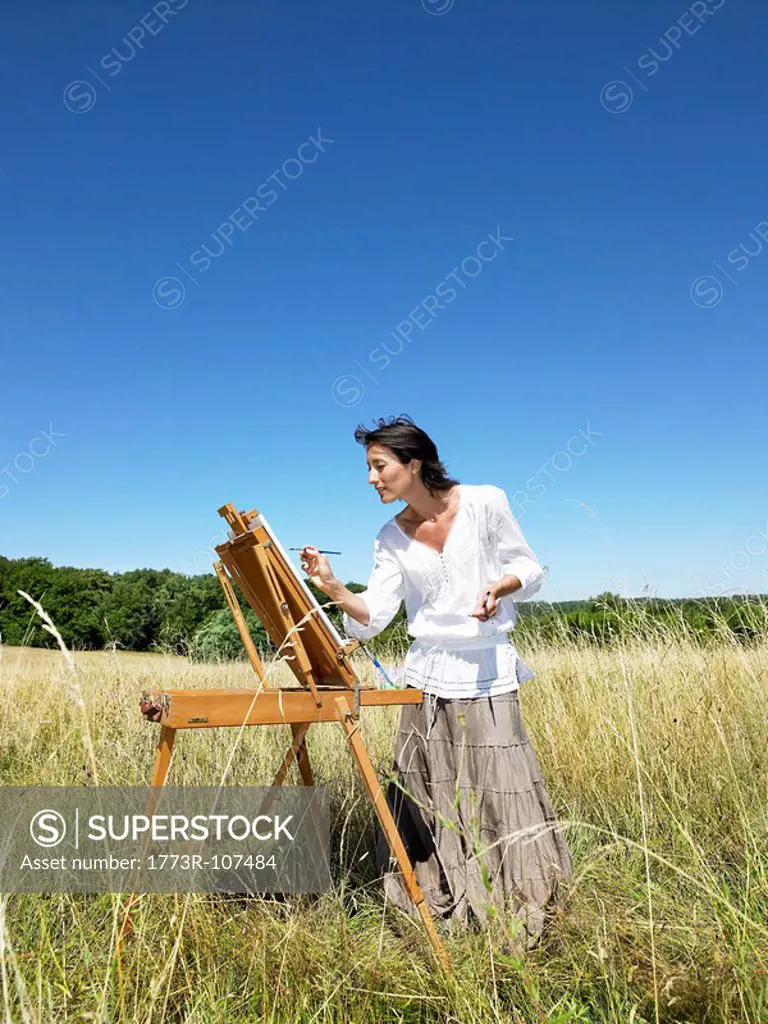 Woman painting in a field, smiling