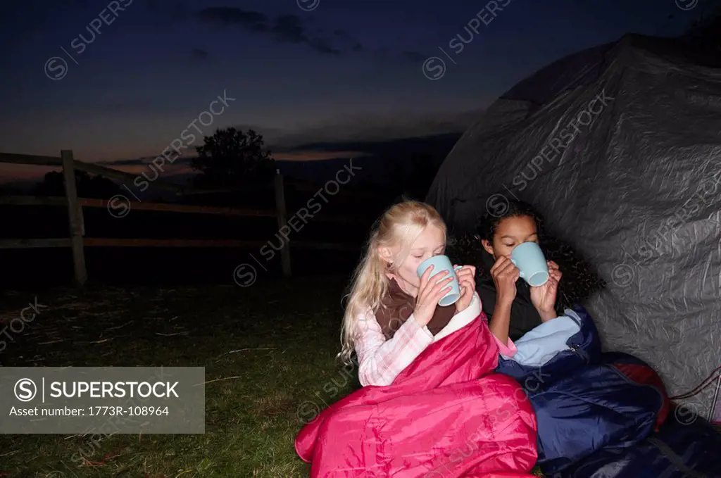 Girls drinking hot drink near tent