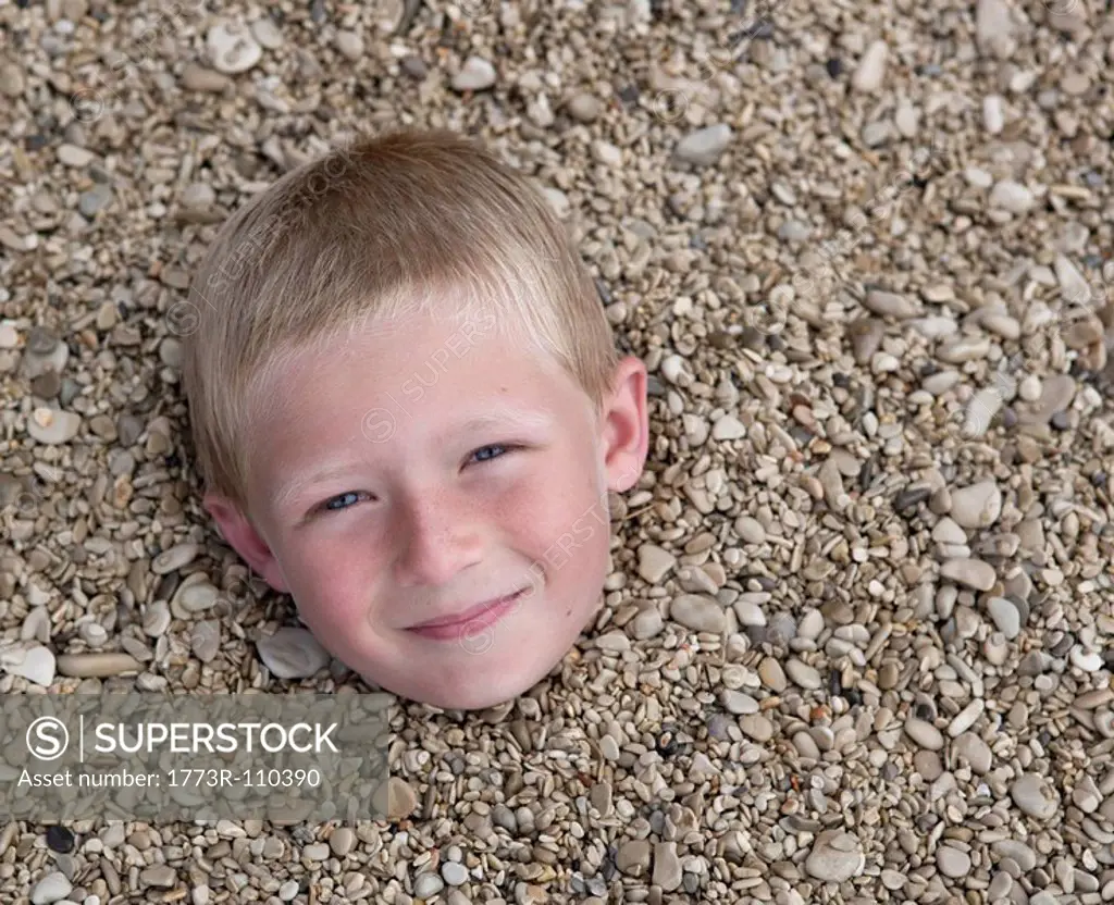 Boy buried in pebbles on beach