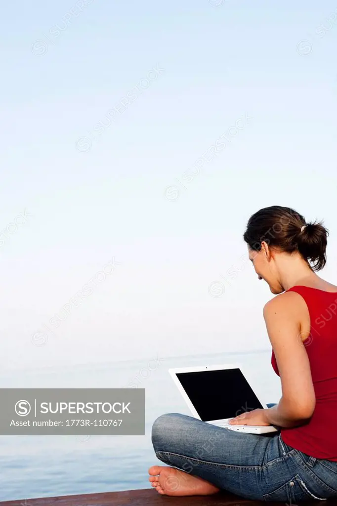 Young Woman On Jetty Looking At Laptop