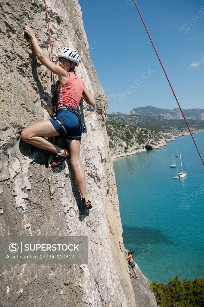 Woman rock climbing, bay in background