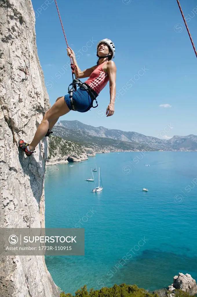 Woman rock climbing, bay in background
