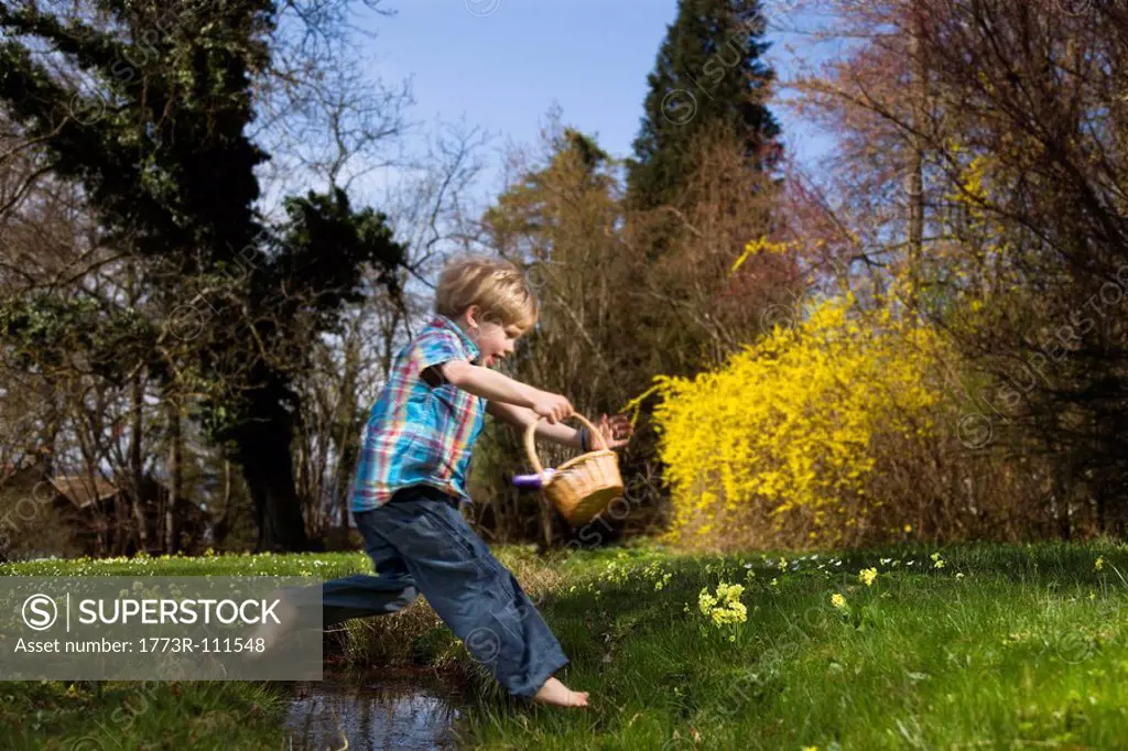 boy jumping over creek holding basket