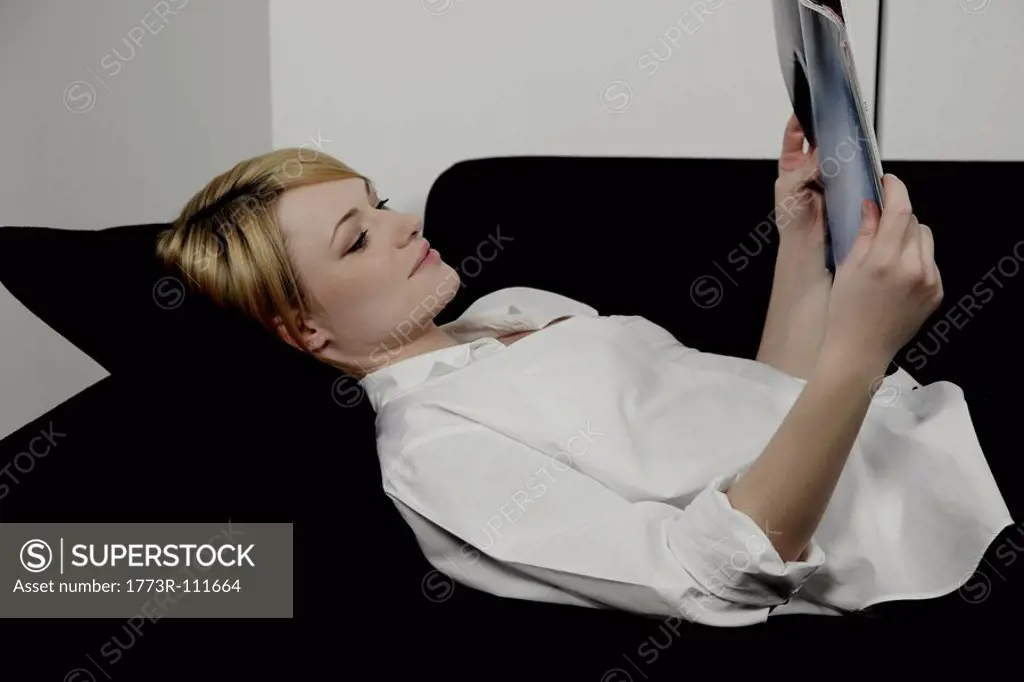 Woman laying on sofa reading magazine.