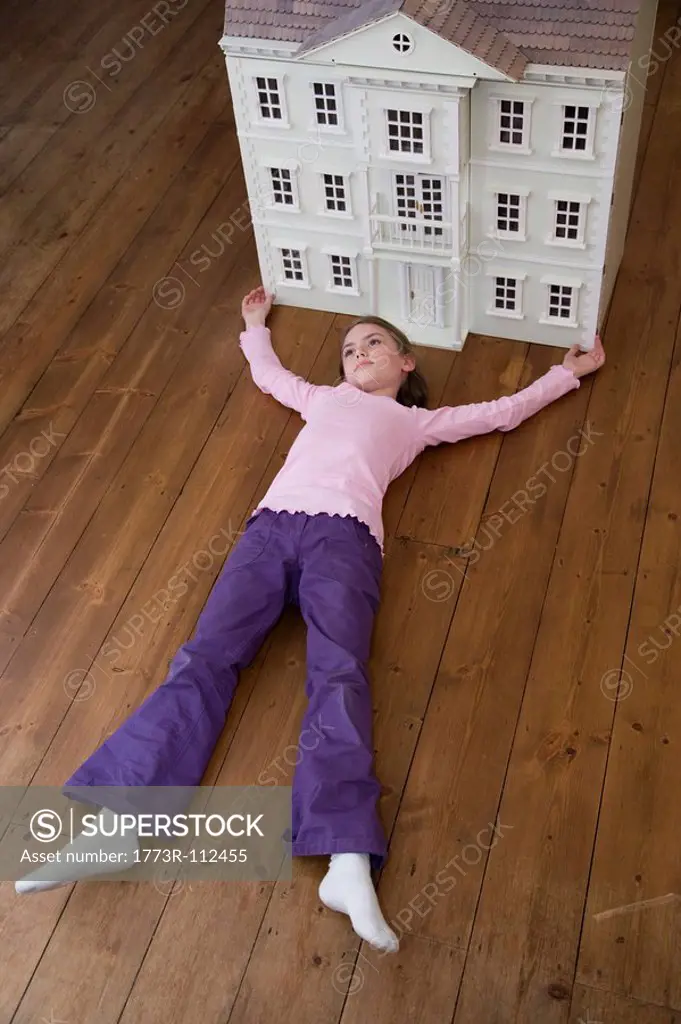 A girl lying in front of her dollhouse.