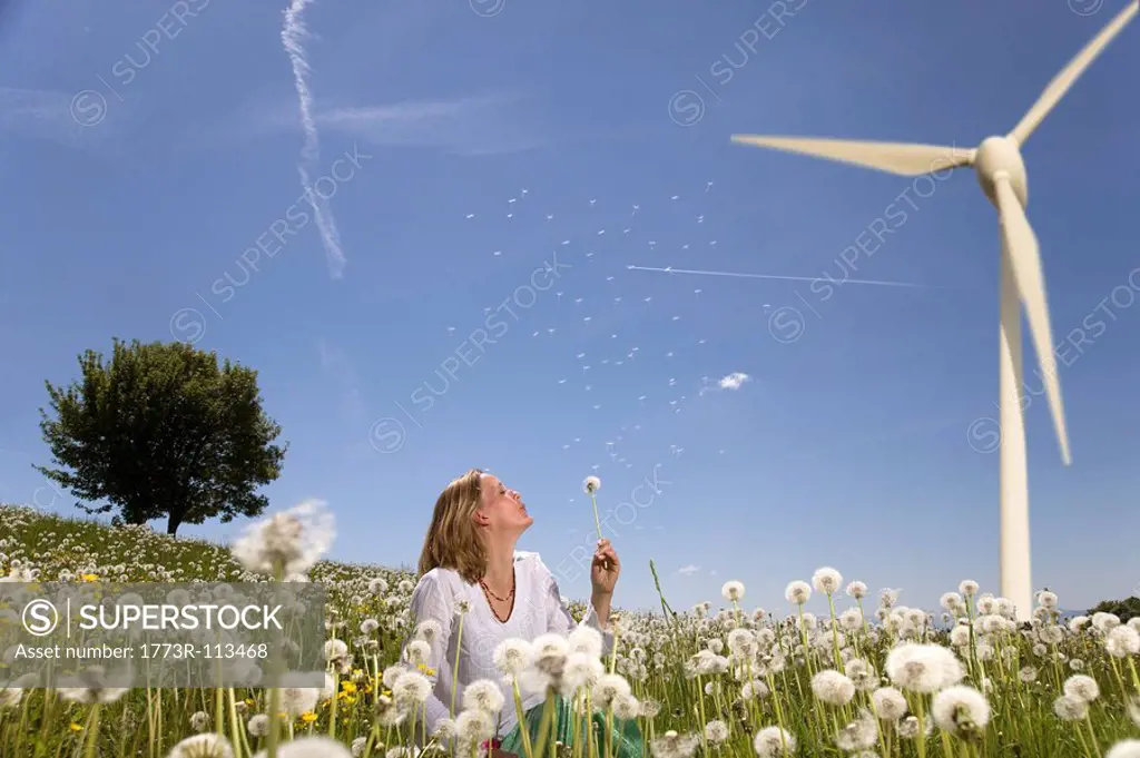woman blowing dandelion at wind turbine
