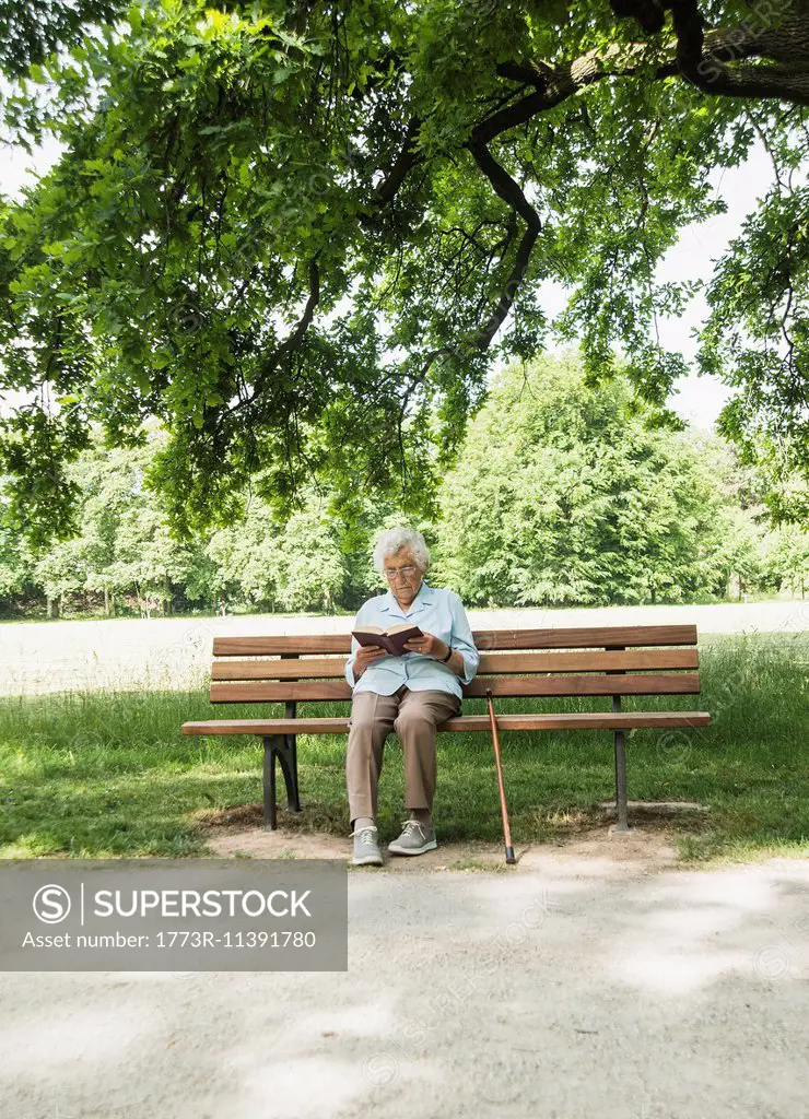 Senior woman sitting on park bench reading bible
