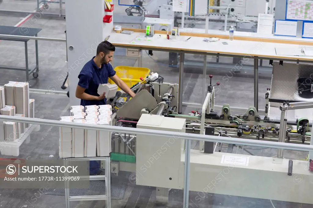 Male worker using machine in paper packaging factory