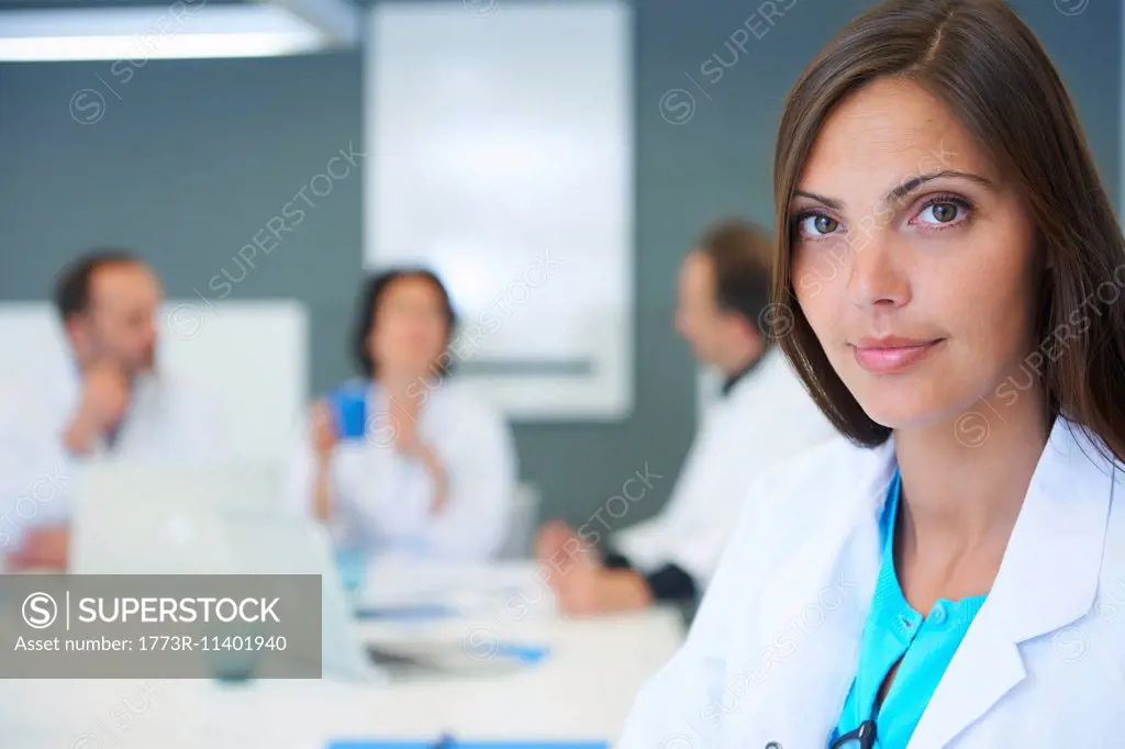 Portrait of female doctor, colleagues having discussion behind