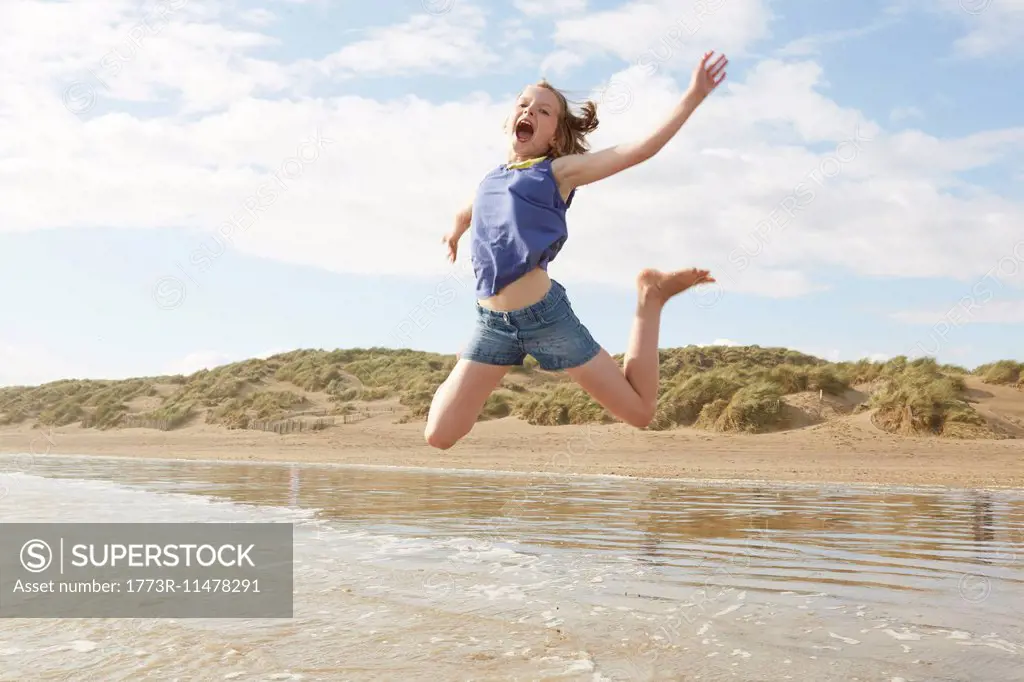 Girl jumping mid air on beach, Camber Sands, Kent, UK