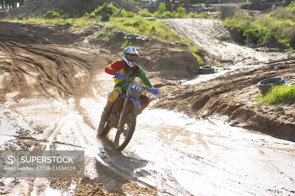 Young male motocross rider racing on muddy track