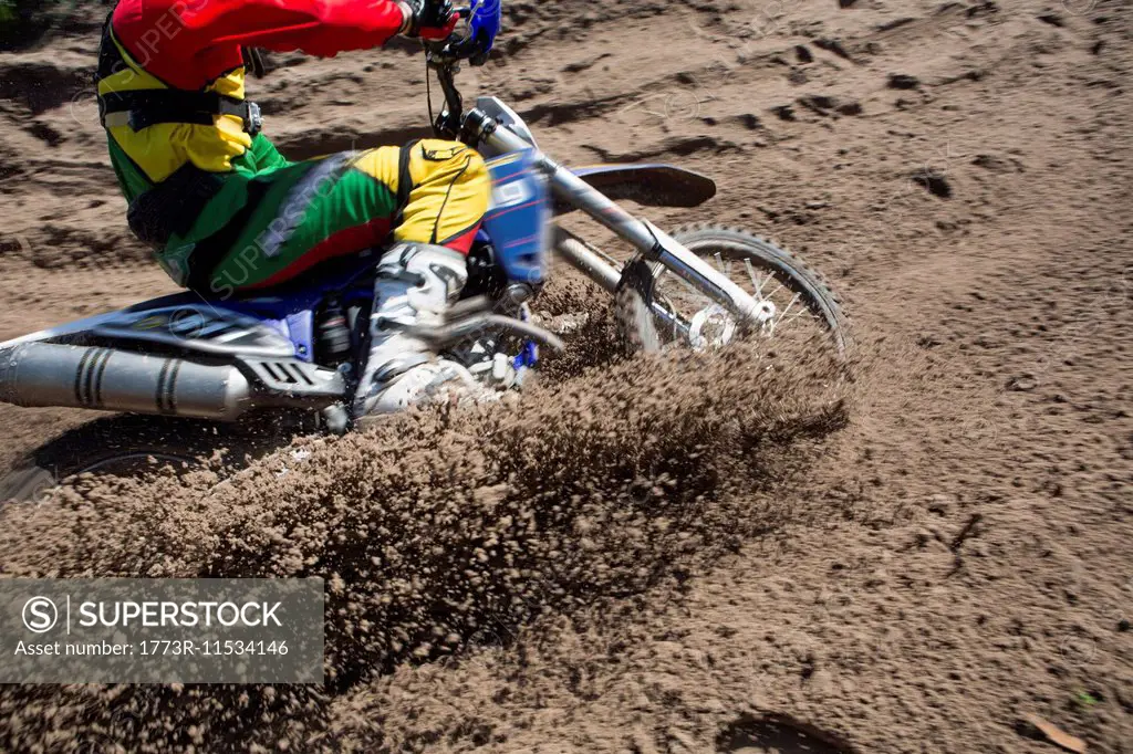 Young male motocross rider racing through mud track