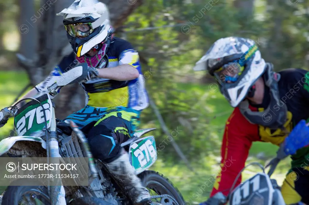 Two young male motocross riders racing through forest