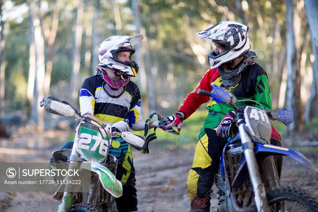 Two young male motocross riders chatting on forest track
