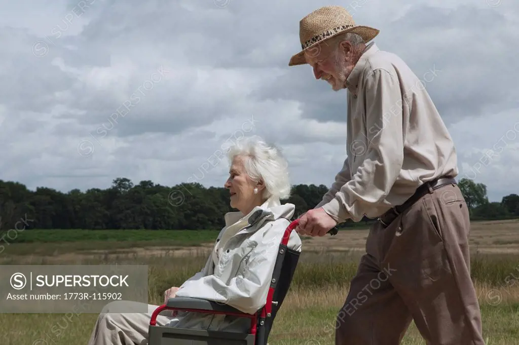 Elderly man pushing woman in wheelchair