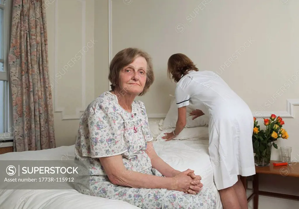 Nurse making bed for elderly woman
