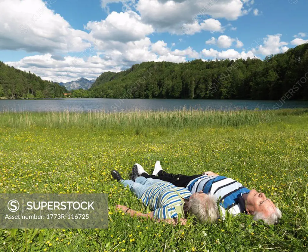 Senior couple lying in field by lake