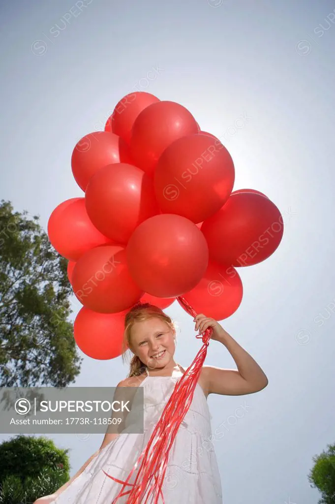 Young girl holding bunch of red balloons