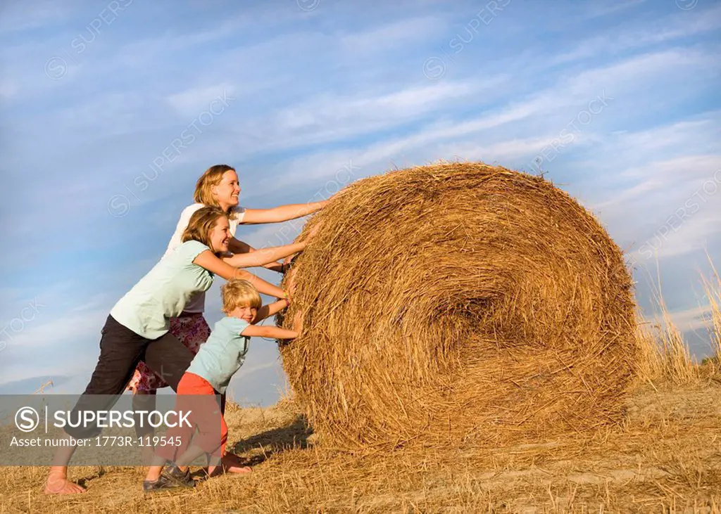 girl, woman, boy pushing hay bale