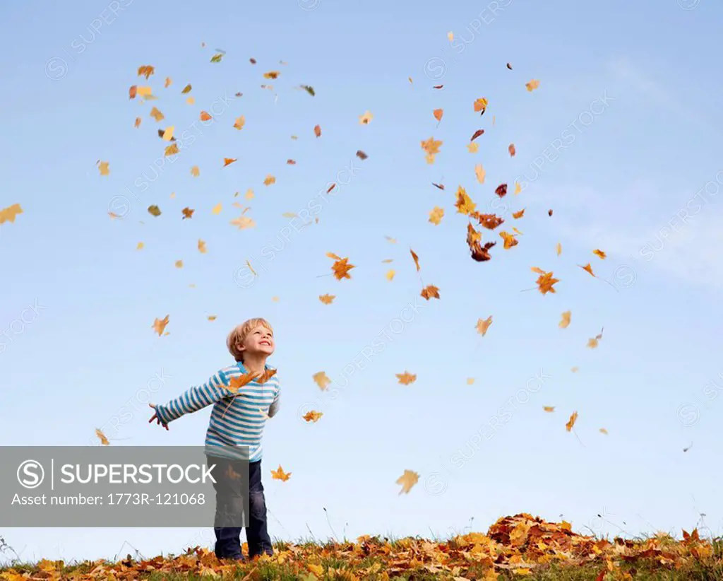 boy throwing autumn leaves into the air