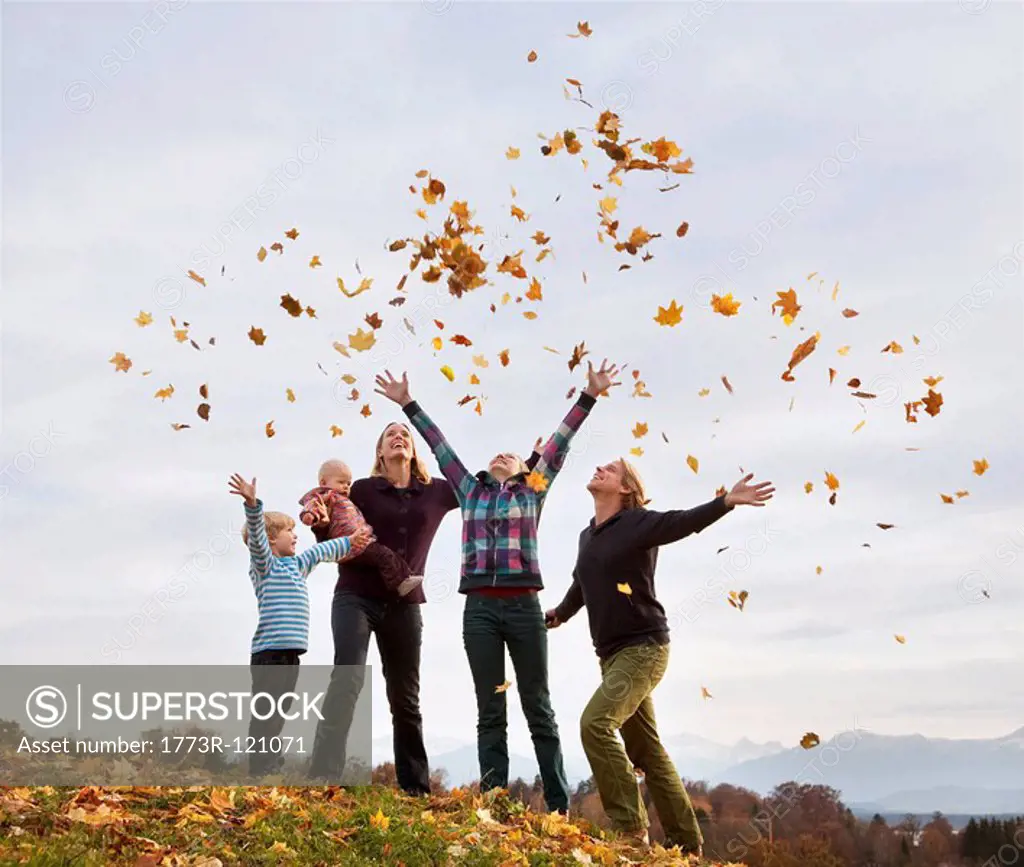 family throwing autumn leaves into air