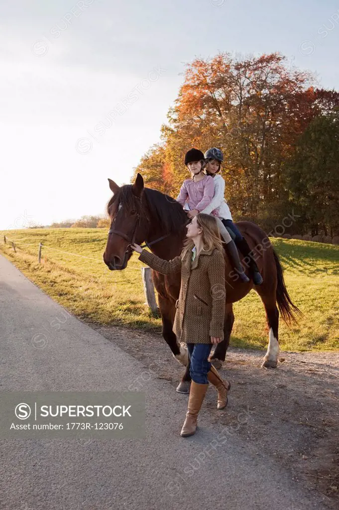 Woman walking a horse with two girls