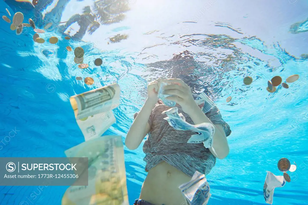 Underwater view of boy in swimming pool grabbing euro currency