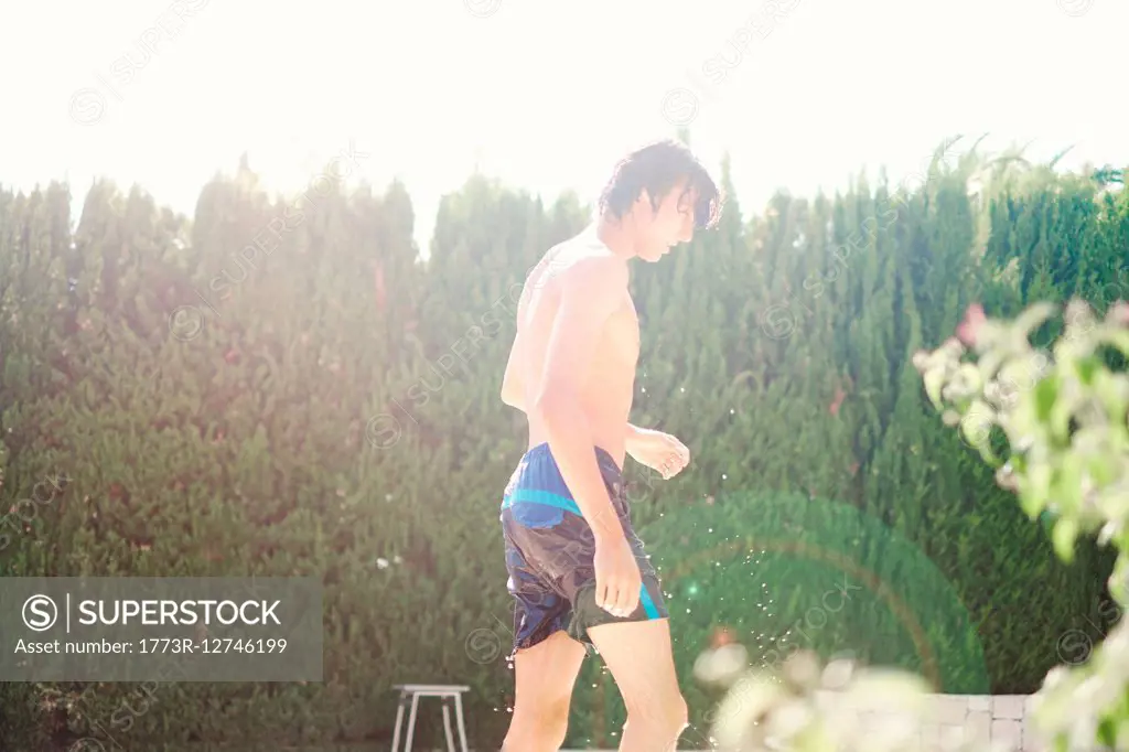 Young man wearing swimming shorts dripping wet at poolside