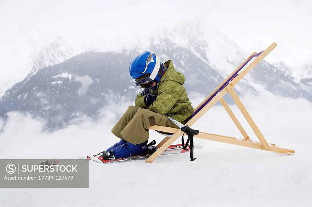 Child with skis sitting on deck chair