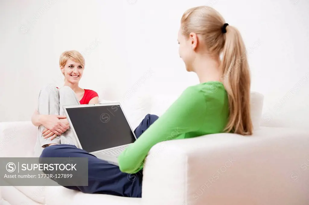 Two women using laptop and phone on sofa