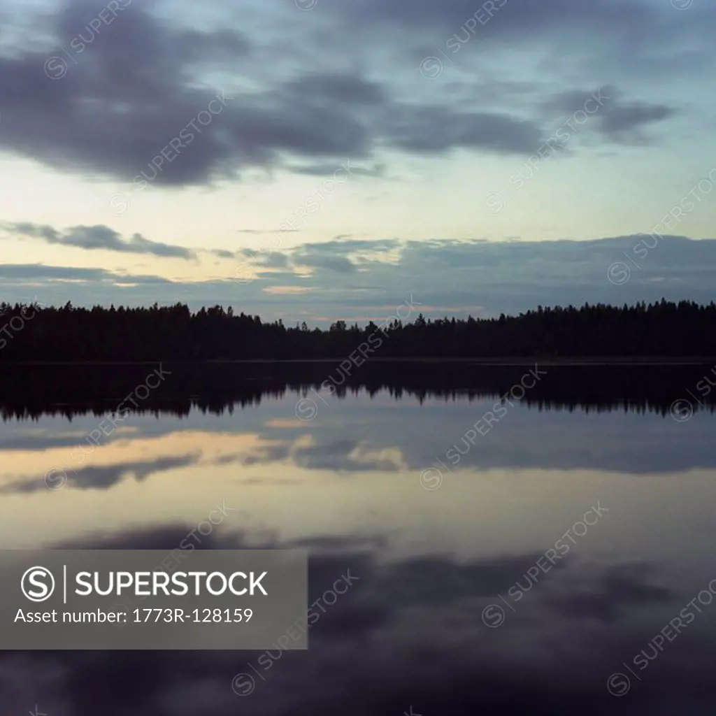 Sky and trees reflected in lake at night