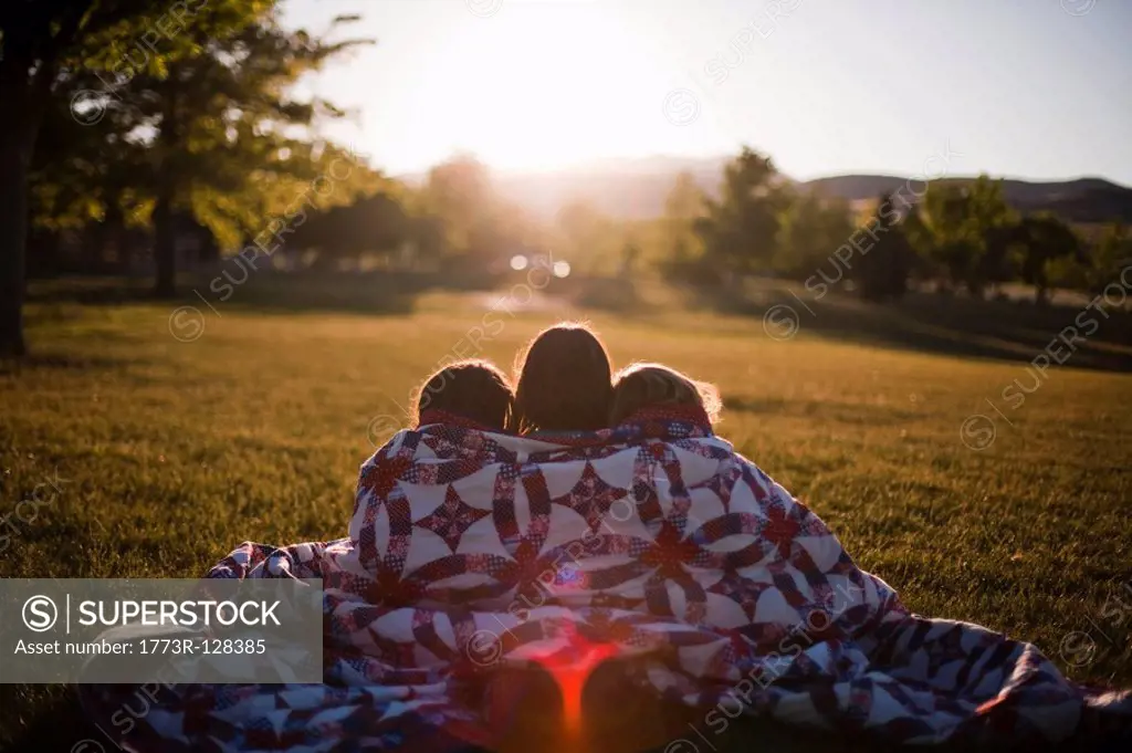 3 girls wrapped in blanket at sunset