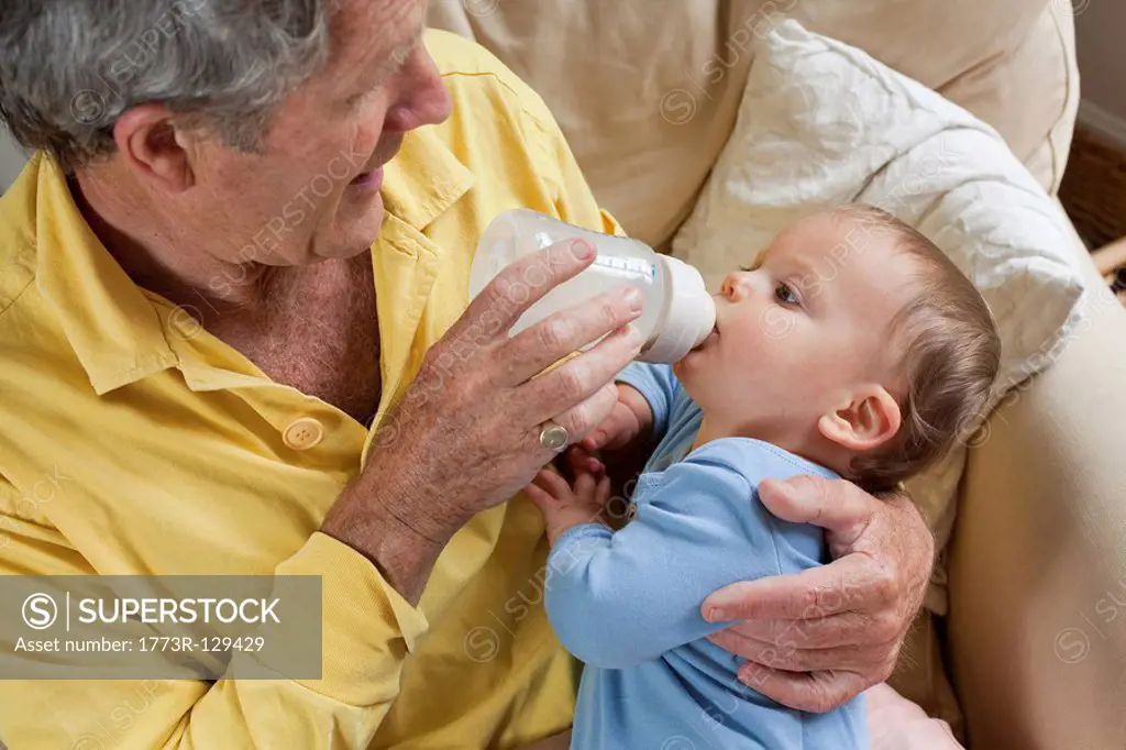 Grandad feeding grandson milk bottle