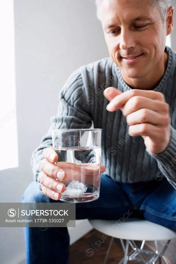Man dropping pill into glass of water