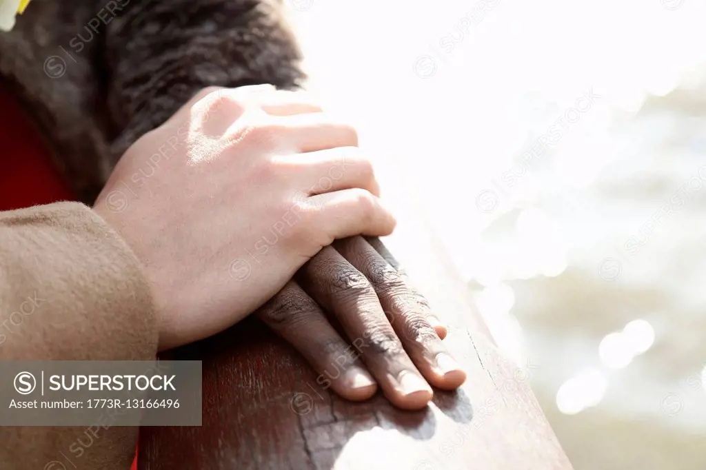 Multi ethnic couple outdoors, man resting hand on woman's hand, close-up