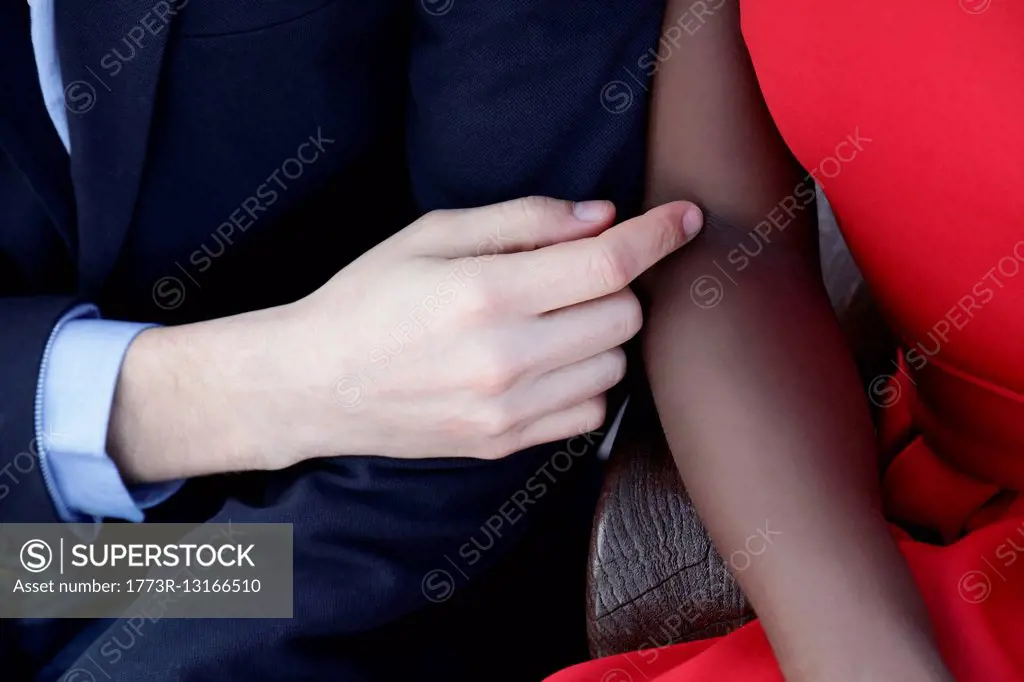 Multi ethnic couple sitting together, man touching woman's arm, mid section, close-up