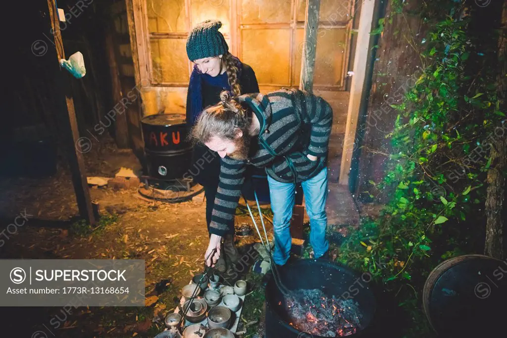 Couple using tongs to remove clay pots from fire, smiling