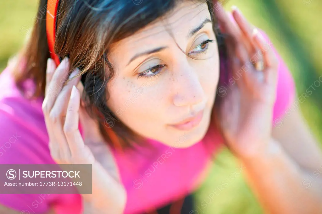 Cropped high angle view of mature woman wearing headphones, hands on ears looking away