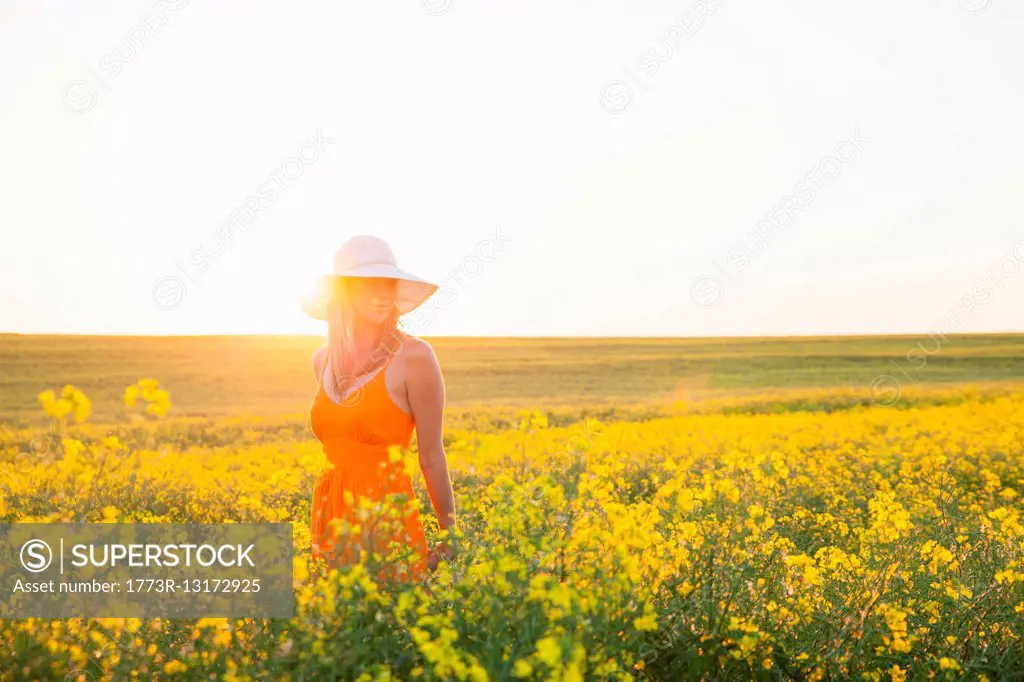 Mid adult woman in canola field wearing sunhat looking away