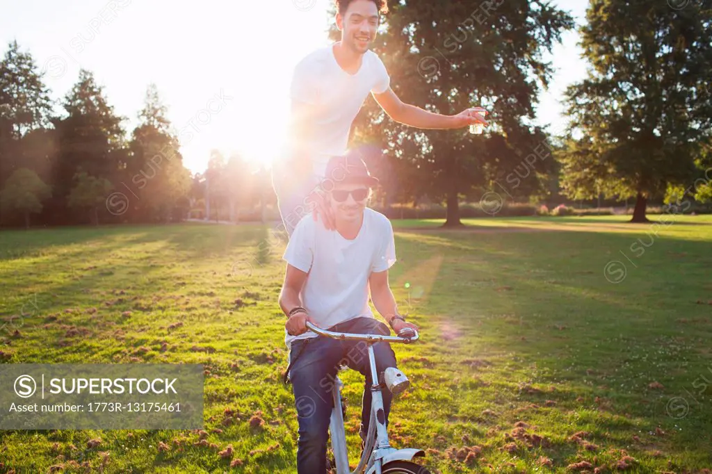 Party going man arriving in park standing on back of bicycle at sunset