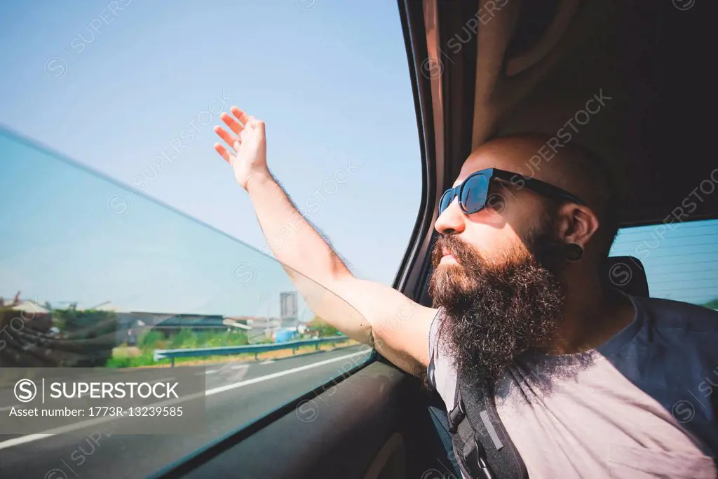 Bearded man sticking hand out of car window on highway, Garda, Italy