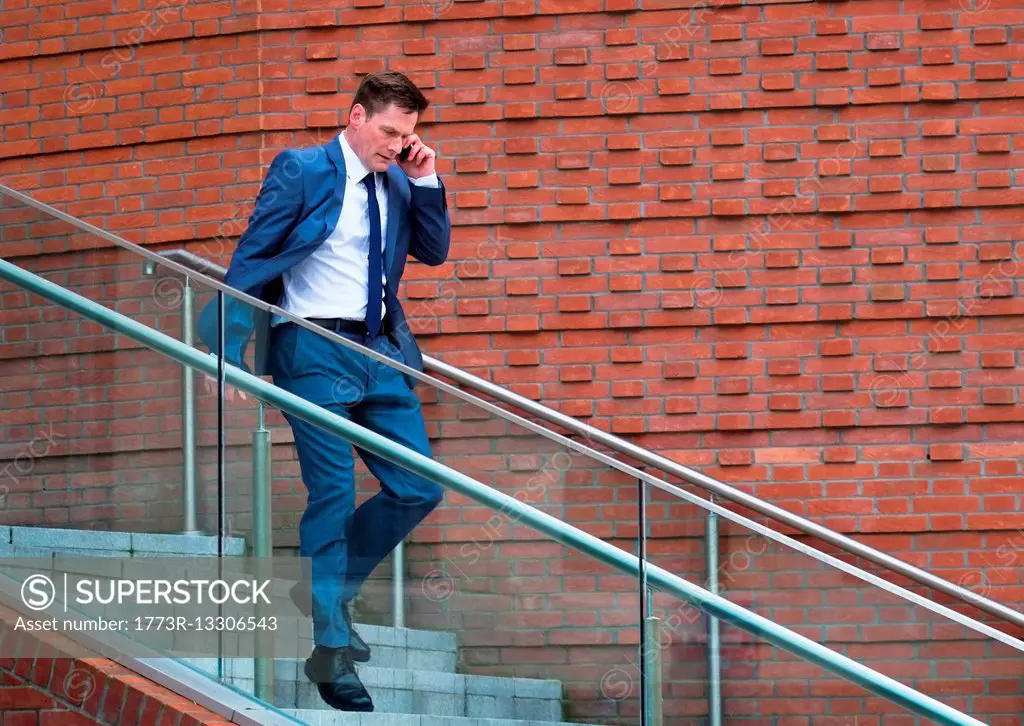 Mature businessman walking down steps, using smartphone