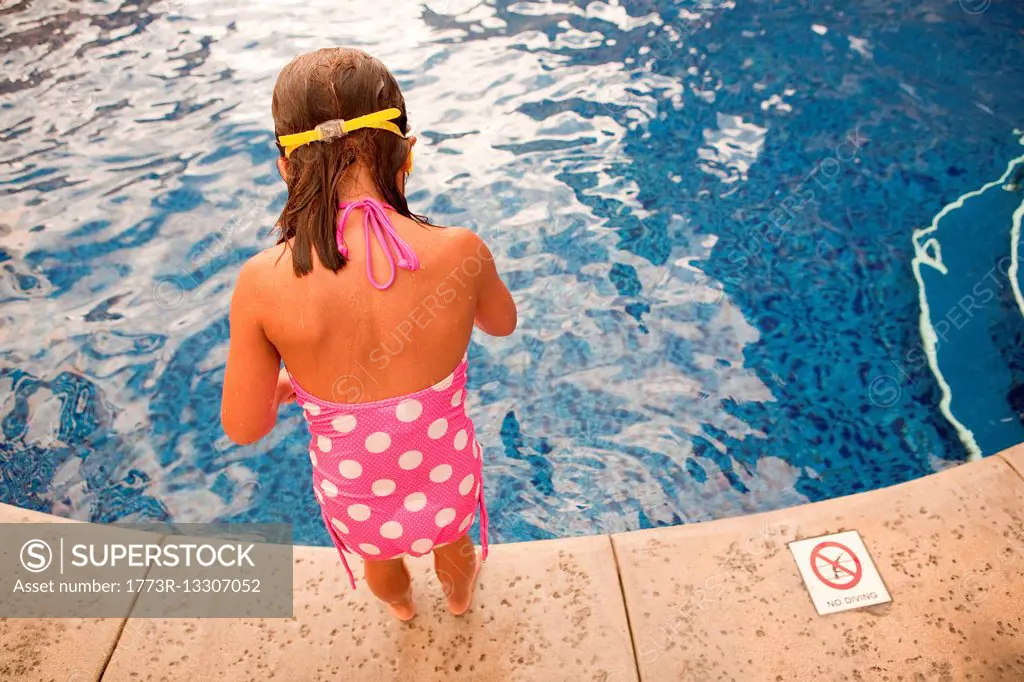 Young girl standing at poolside, high angle